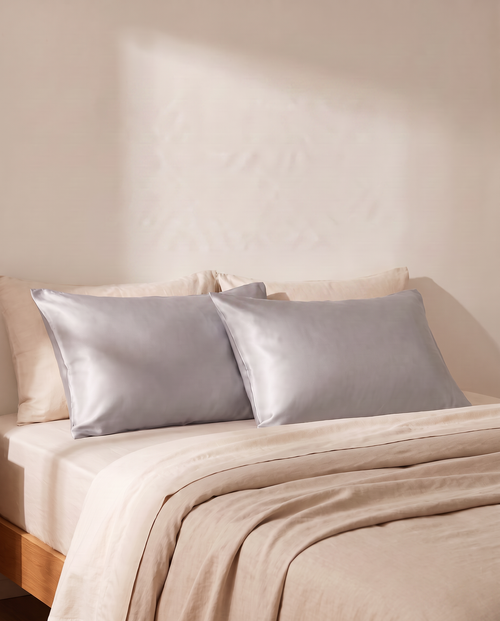 Lullia grey satin cooling pillowcases on an oat-linen bed in soft morning light